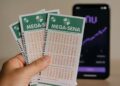 Bilhetes da Mega-Sena, ao fundo o app do Nubank