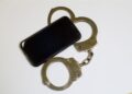 Olhar o celular do parceiro sem permissão pode dar cadeia? Um celular ao lado de uma algema