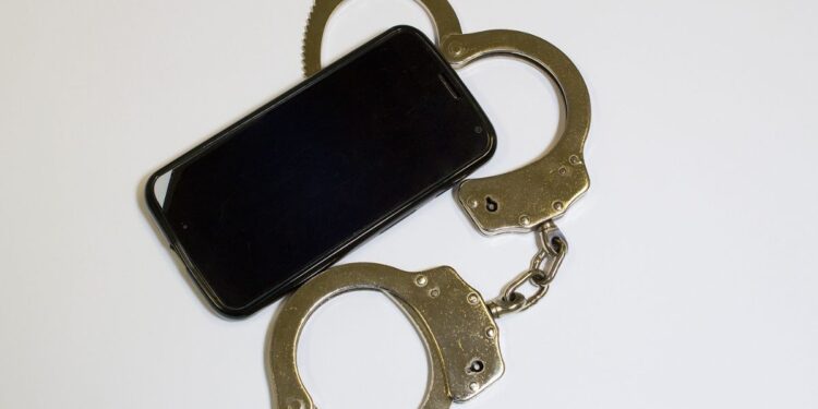 Olhar o celular do parceiro sem permissão pode dar cadeia? Um celular ao lado de uma algema