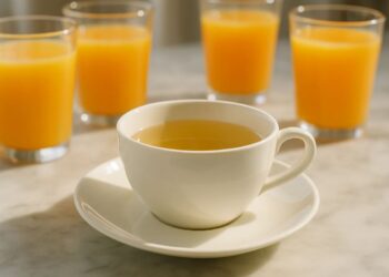 Uma xícara de chá branco, ao fundo 4 copos de suco de laranja