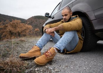 Um motorista sentado ao lado do pneu do seu carro ao pensar que a estrada estaria vazia