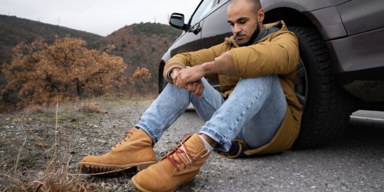 Um motorista sentado ao lado do pneu do seu carro ao pensar que a estrada estaria vazia