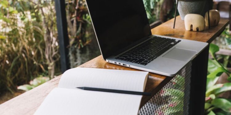 Notebook sem carregador em uma mesa com caderno e lápis aberto no meio