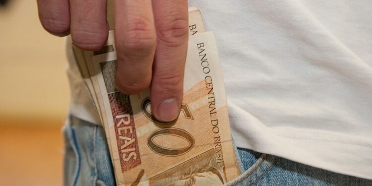 Uma pessoa coloca notas de 50 reais do PIS e PASEP