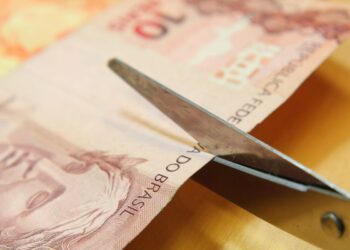 Nota de 10 reais sendo cortada representando o salário mínimo 2026