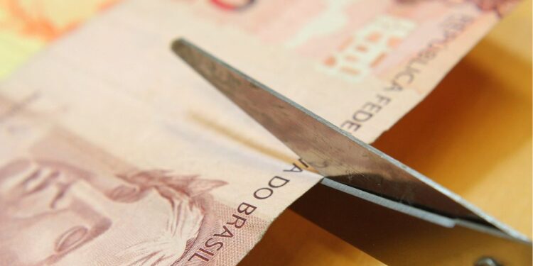 Nota de 10 reais sendo cortada representando o salário mínimo 2026