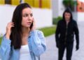 Uma mulher fala ao celular antes de fazer um Boletim de Ocorrência online, enquanto é perseguida por um homem