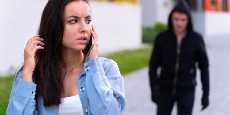 Uma mulher fala ao celular antes de fazer um Boletim de Ocorrência online, enquanto é perseguida por um homem