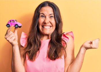 Uma mulher feliz com a isenção do IPVA 2026 segura uma miniatura de carro rosa