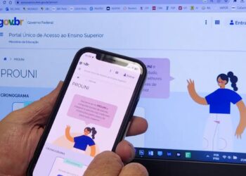 Uma pessoa segura o aplicativo em frente ao site do ProUni