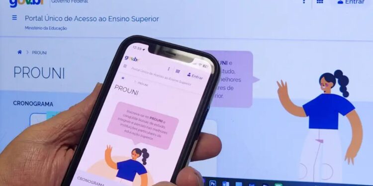 Uma pessoa segura o aplicativo em frente ao site do ProUni