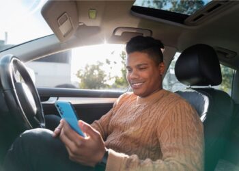 Motorista com celular na mão dentro do carro feliz depois de ver o PIX no seu celular