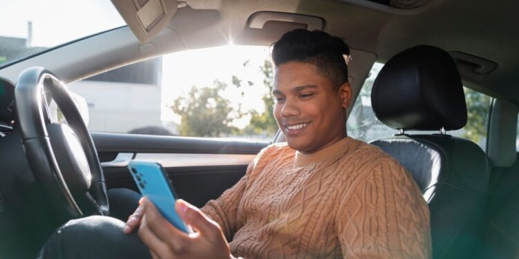 Motorista com celular na mão dentro do carro feliz depois de ver o PIX no seu celular