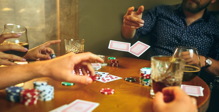 Foto da vista lateral de amigos sentados à mesa de madeira. Amigos se divertindo enquanto jogam o jogo de tabuleiro.