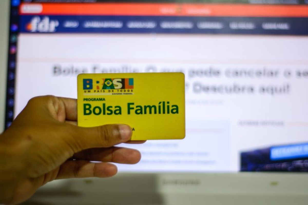 Um Titular do Bolsa Família com o cartão amarelo do benefício em frente ao computador