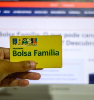 Um Titular do Bolsa Família com o cartão amarelo do benefício em frente ao computador