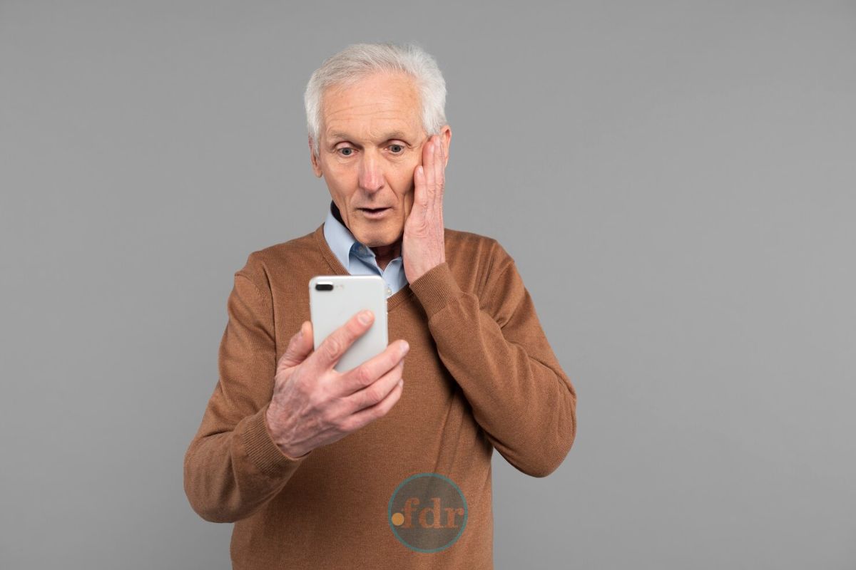 Um senhor assustado, ele olha para seu celular e vê que houve u, desconto indevido no INSS