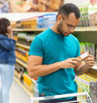 Um homem olha o rótulo do produto em sua mão após ver que a Cesta básica ideal custa R$ 432