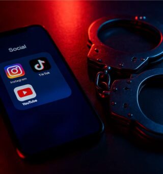 Uma algema ao lado de um celular representando a prisão de Influenciadores Digitais