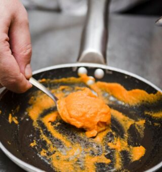 Uma pessoa tirando um creme laranja da frigideira com uma colher