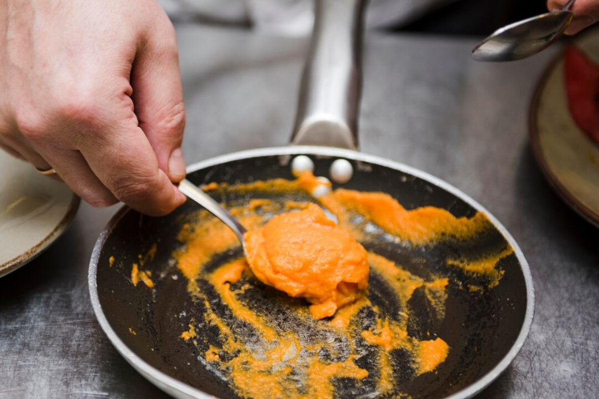 Uma pessoa tirando um creme laranja da frigideira com uma colher