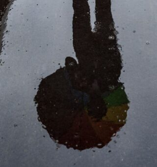 Uma pessoa com guarda-chuva sendo vista no reflexo de uma poça de água de chuva, sentindo o petricor
