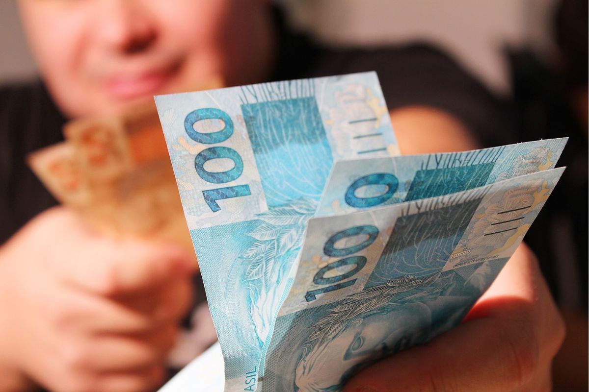 Uma mão segura notas de R$ 100 do Empréstimo com garantia de imóvel