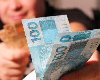 Uma pessoa segura notas de R$ 100 referentes ao abono salarial de 2026