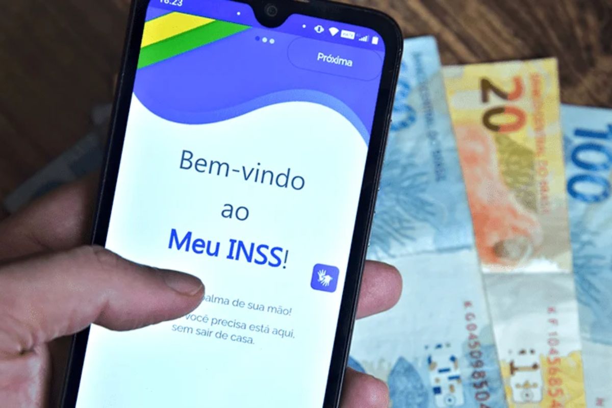 Aplicativo Meu INSS em um celular com notas de reais embaixo