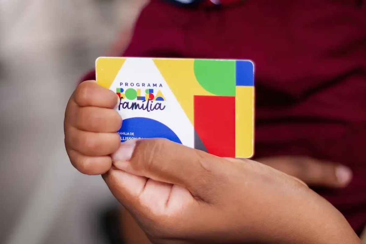 Uma criança no colo da mãe segura o cartão do Bolsa Família
