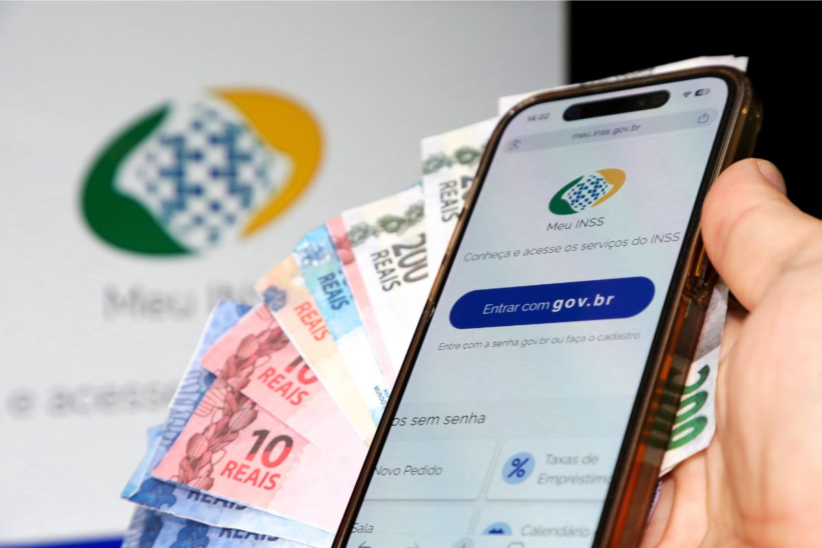 Uma pessoa com o aplicativo do INSS no celular (em sua mão), junto com algumas notas de reais