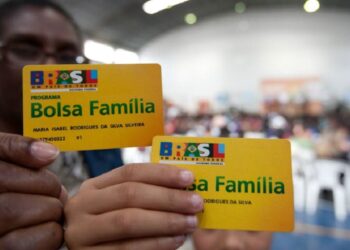 Uma mãe segura o cartão do Bolsa Família e sua filha outro