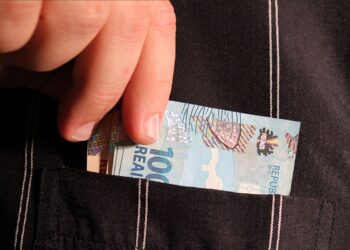 Uma pessoa classe média guarda uma nota de real no bolso
