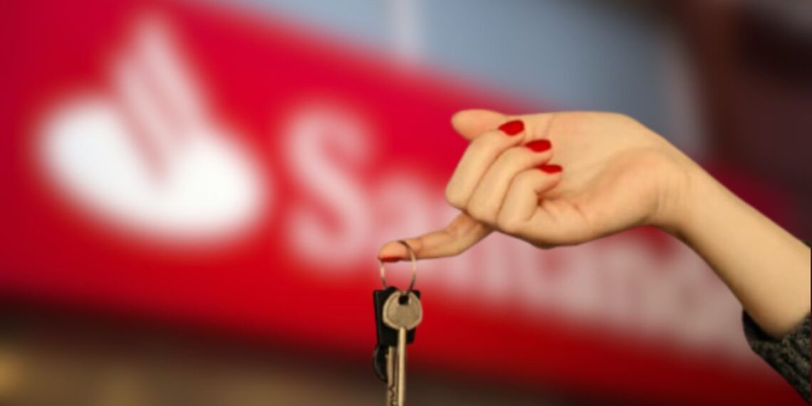 Uma mão segura a chave após o leilão com o logo do Santander ao fundo