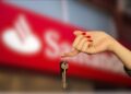 Uma mão segura a chave após o leilão com o logo do Santander ao fundo