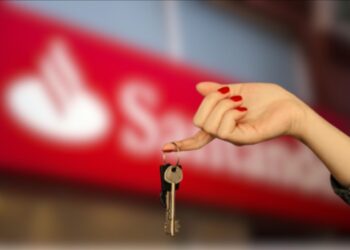 Uma mão segura a chave após o leilão com o logo do Santander ao fundo