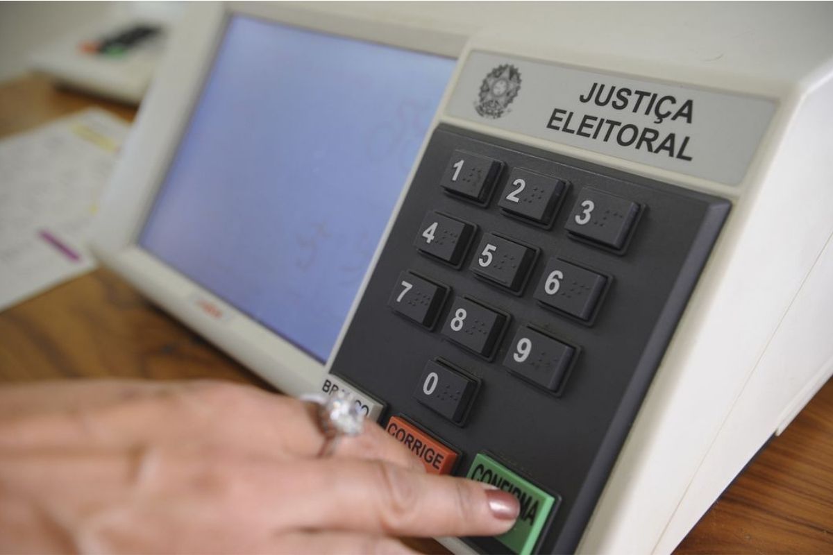 Uma mão de mulher apertando 'confirma' na urna eletrônica 